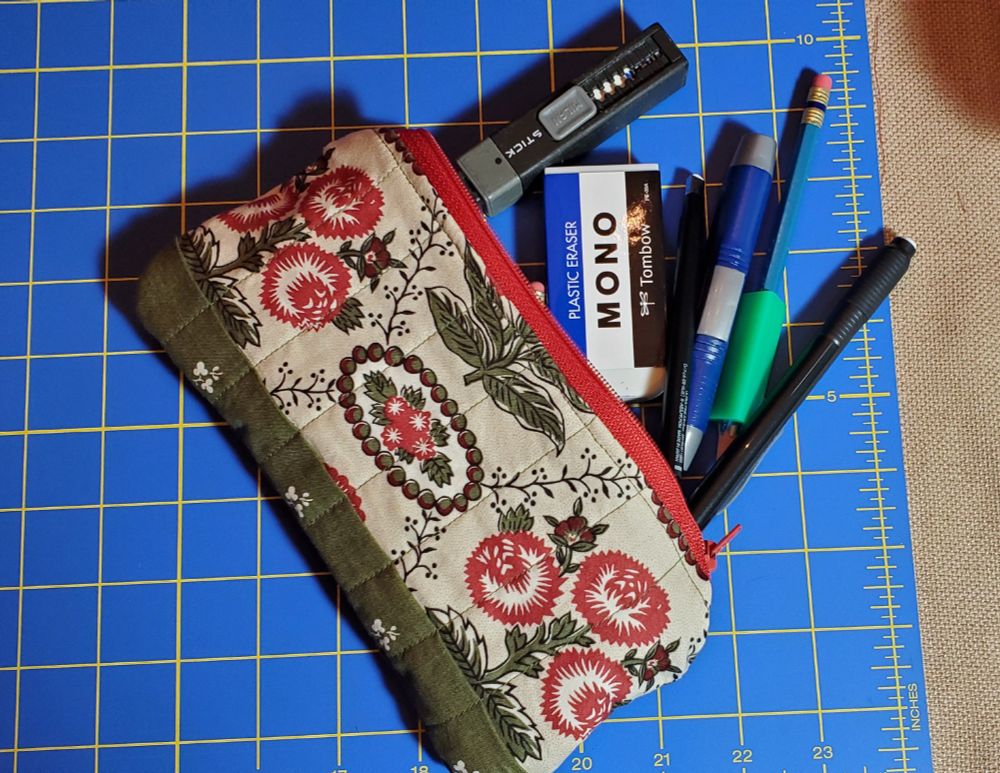 A photo of a quilted pencil case in floral fabric. Pencils and erasers are spilling out of the case.