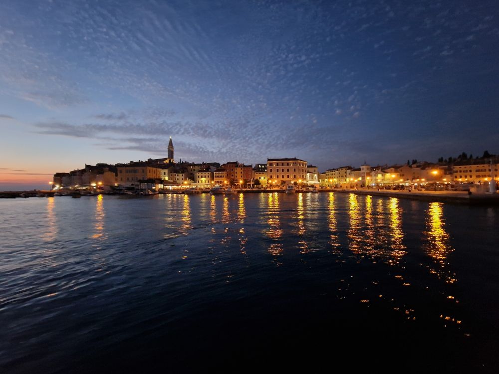 Rovinj am Abend. Im Vordergrund das Meer indem sich die Lichter spiegeln