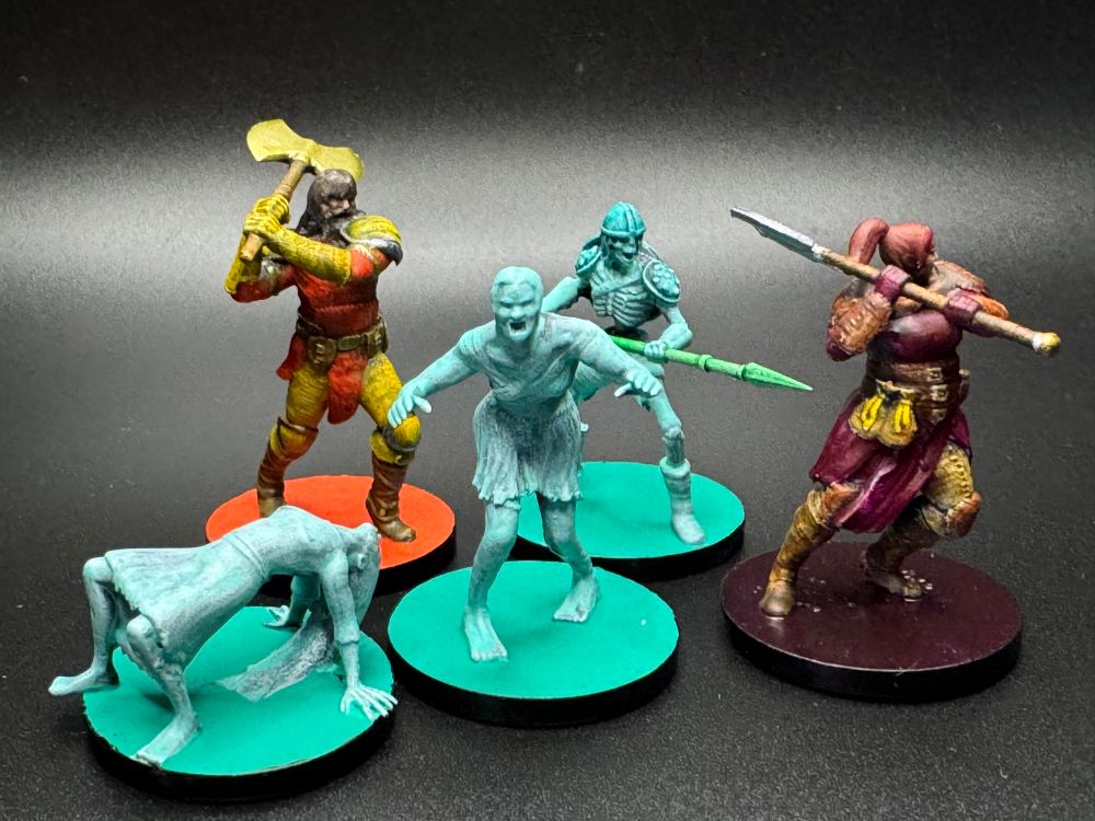Five painted miniatures. Two are barbarians, one in a burgundy color scheme and the other in orange and yellow. The remaining three are a zombie, skeleton, and possessed person (?) done up with ethereal paint to make them look ghostly