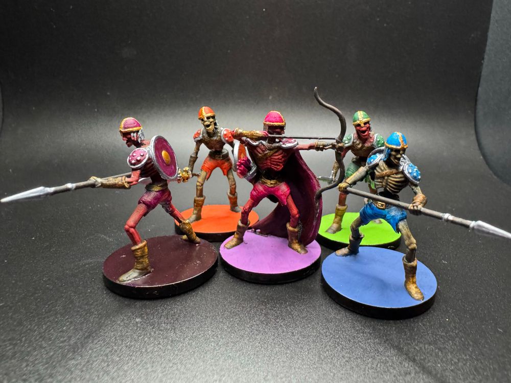 Five painted skeleton miniatures in green, blue, burgundy, orange, and pink