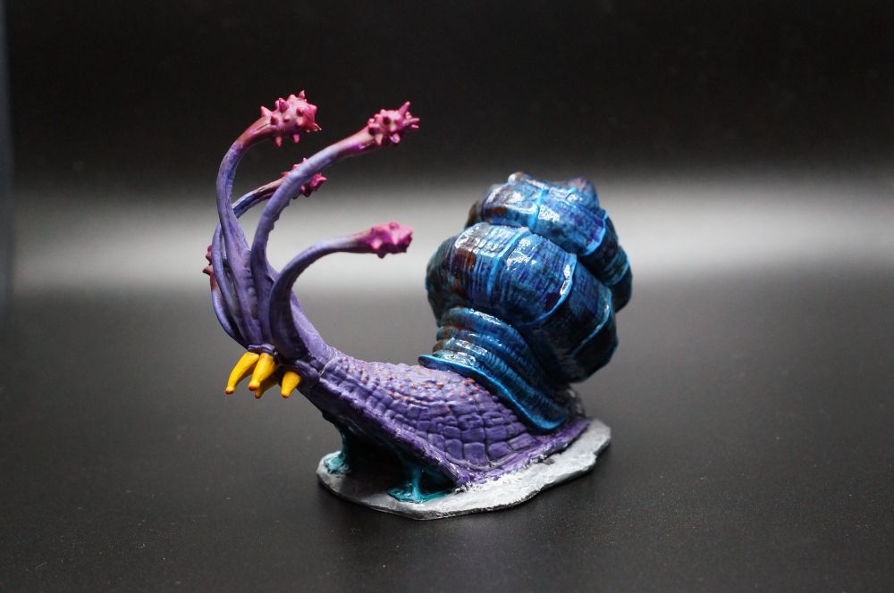 A painted miniature of a Flail Snail, a D&D magical snail with flail antennae and an antimagic shell. I have painted it in a sort of Super Metroid-y color scheme with a purple body, blue shell, magenta antennae, yellow tentacles, and a frosty winter base.
