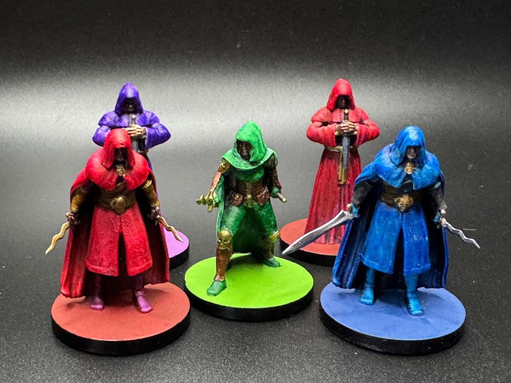 Five painted miniatures of rogues/cultists/assassins. They are painted with blue, green, red, and purple hoods/cloaks/robes