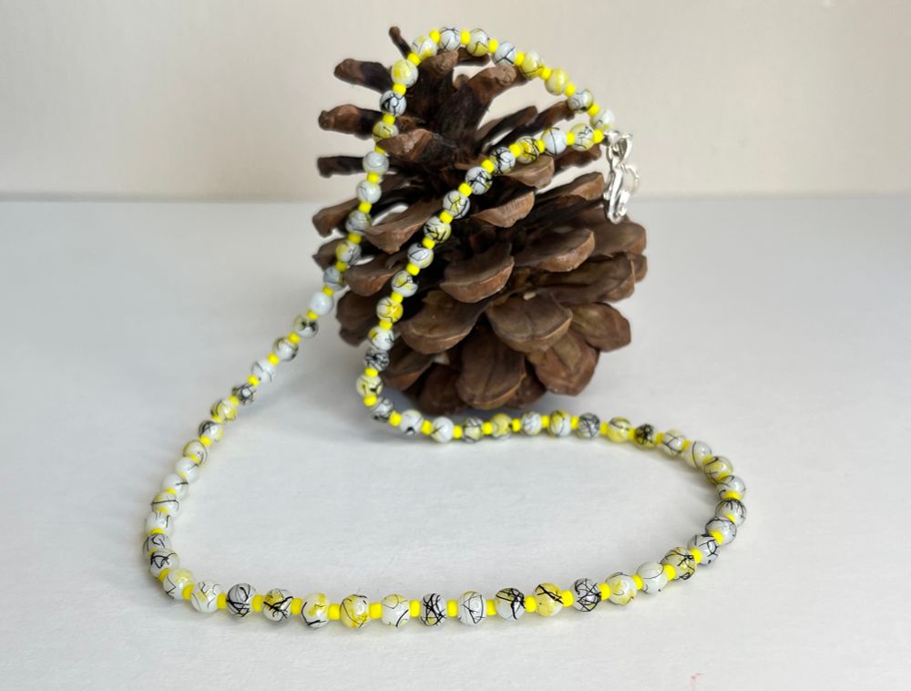A string of Yellow,black and white glass beads draped over a pine cone- 