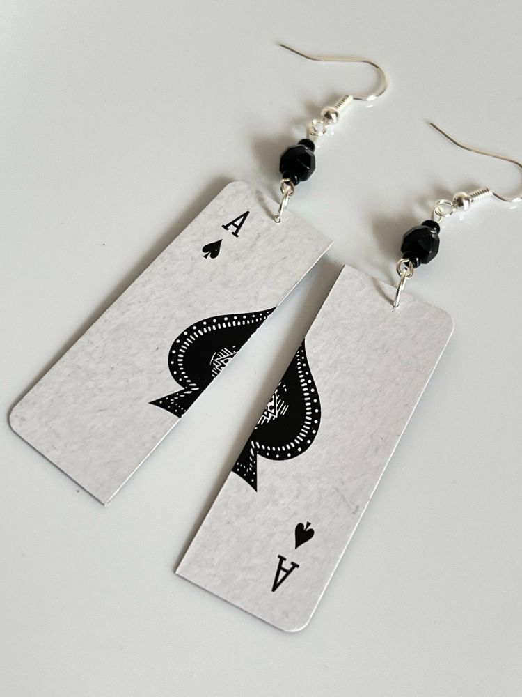 A pair of earrings made with the Ace of Spades playing card from a pack of Christmas cracker playing cards. 
The card has been cut in half lengthwise and each half is linked to a silver plate earhook with black glass beads 