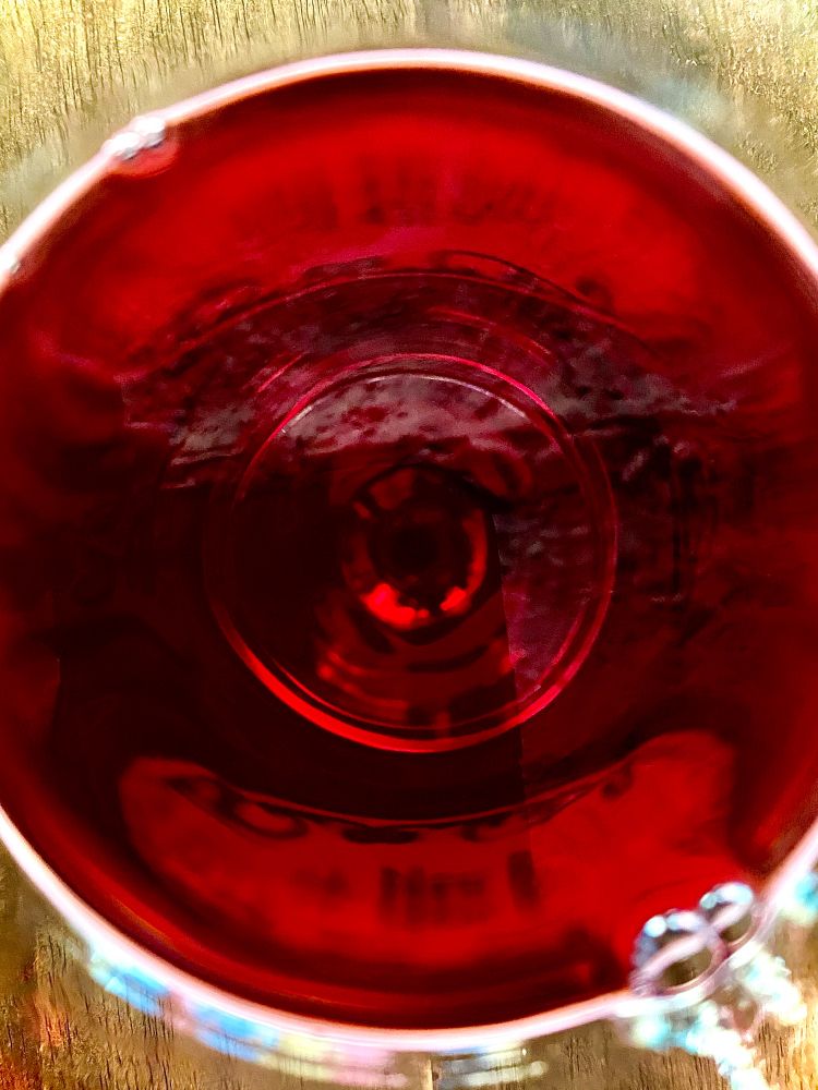 Deep red circle surrounded by a white rim. Wine in a glass from the top down. 