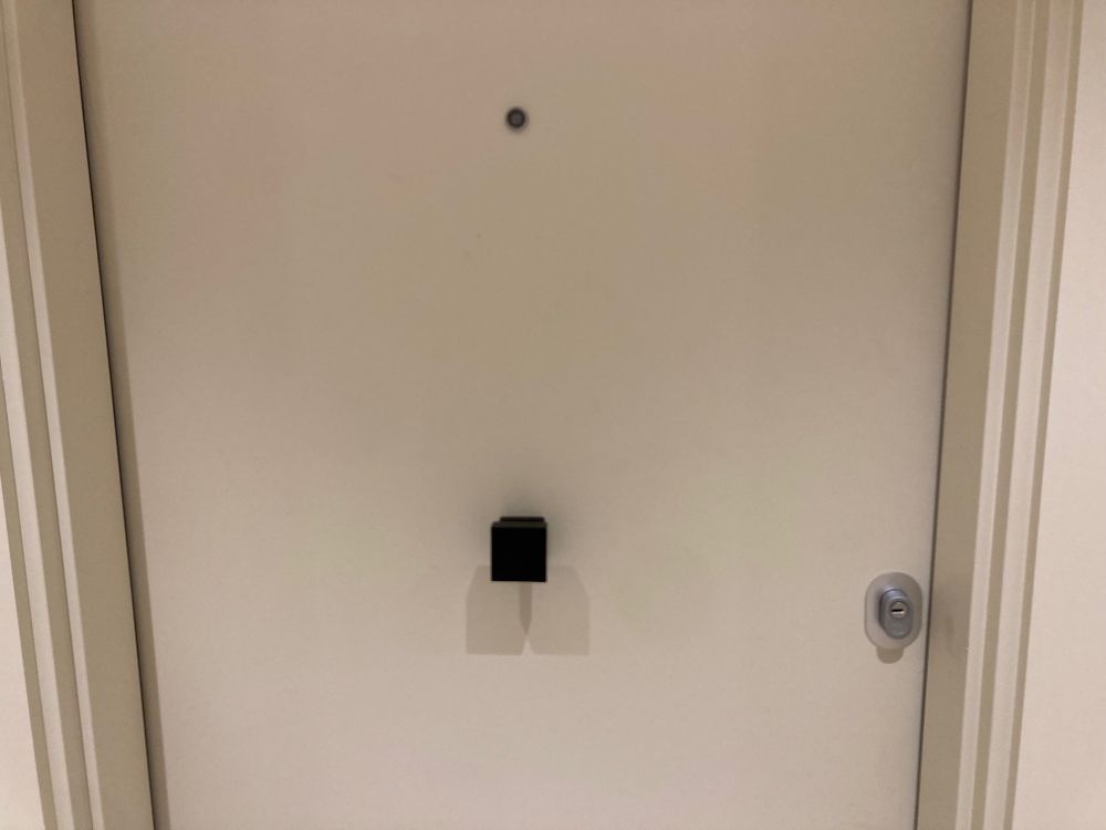 Porte d’appartement beige avec la serrure à droite et un carré-poignée noir au milieu de la porte