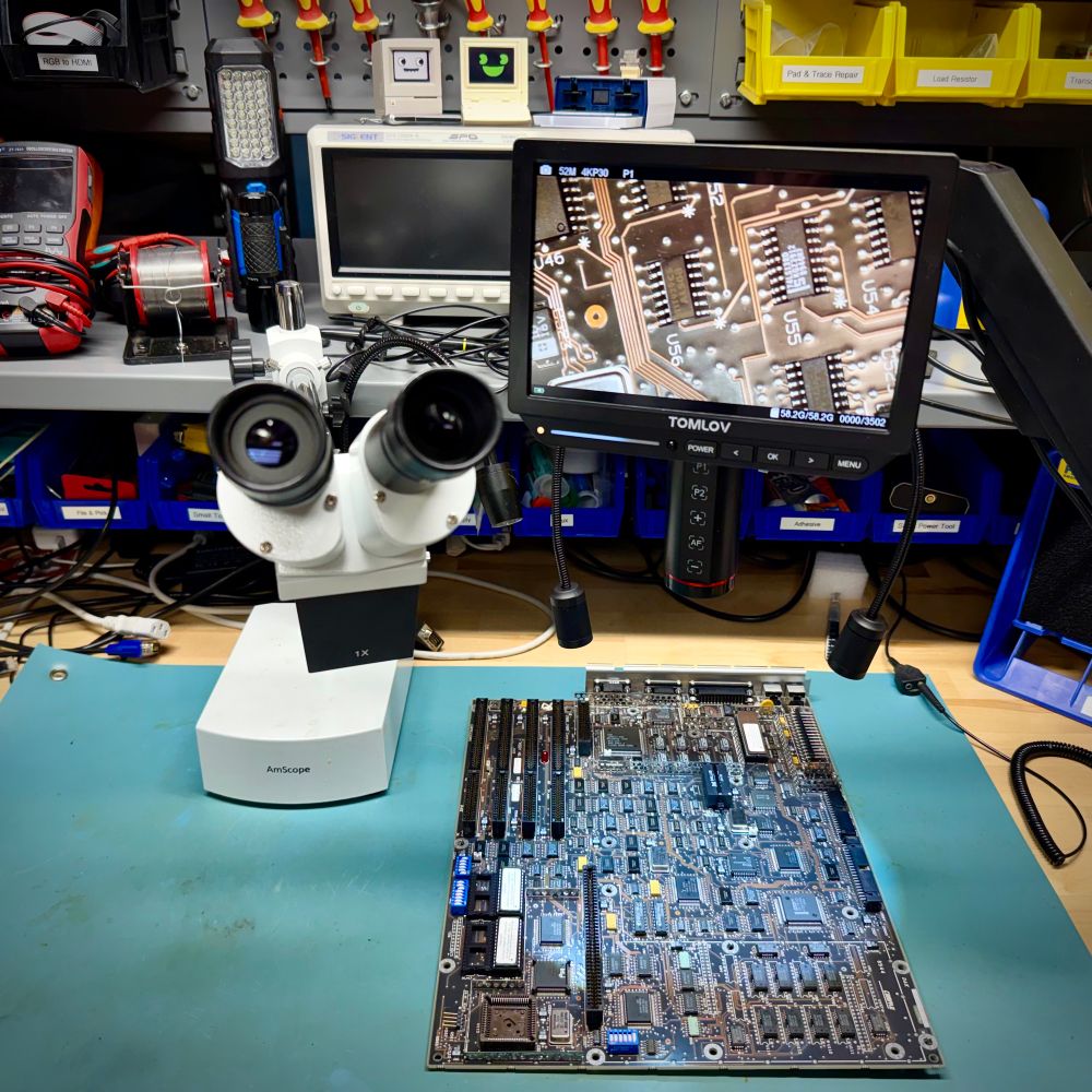 A workbench with a large motherboard and a pair of microscopes