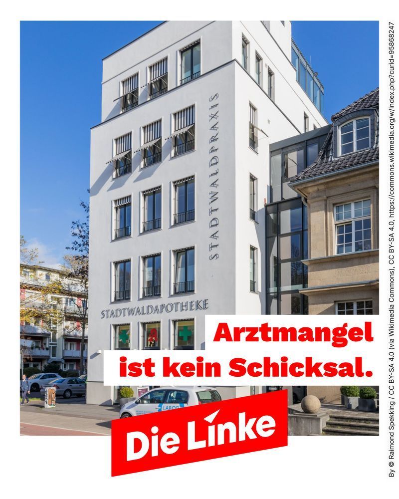 Das Sharepic zeigt ein modernes weißes Ärztehaus mit der senkrechten Beschriftung „STADTWALDPRAXIS“ an der rechten Gebäudekante und der Aufschrift „STADTWALDAPOTHEKE“ über drei großen Schaufenstern im Erdgeschoss. In den Fenstern sind grüne und rote Apothekensymbole zu sehen. Das Gebäude hat mehrere Etagen, große rechteckige Fenster und graue Markisen. Davor stehen ein silberner Kleinwagen mit einem blauen Labor-Aufkleber und weitere geparkte Autos. Links im Hintergrund befinden sich mehrstöckige Wohnhäuser, rechts ein älteres Gebäude mit beigem Sandstein und grauem Ziegeldach. Der Himmel ist klar blau, einige Bäume haben herbstlich gelb gefärbtes Laub. Auf dem unteren Bildbereich steht in großer roter Schrift: „Arztmangel ist kein Schicksal.“ Darunter befindet sich das rote Logo „Die Linke“ auf einer schrägen weißen Fläche.