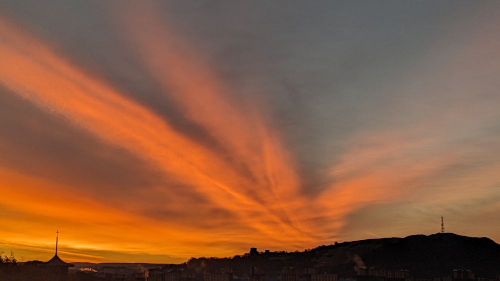 Brilliant orange strips of cloud above the dark silhouette of a hill in the horizon