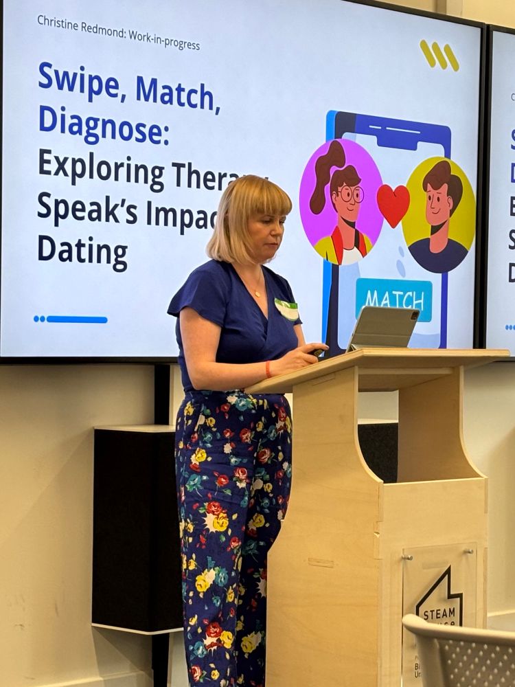 Christine Redmond presenting her research proposal on therapy speak in online dating standing at a podium in front of her opening slide
