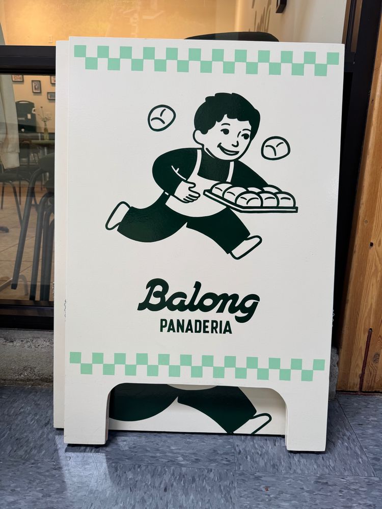 A sign showing a man running with a tray of bread rolls. Underneath words say Balong Panaderia. 