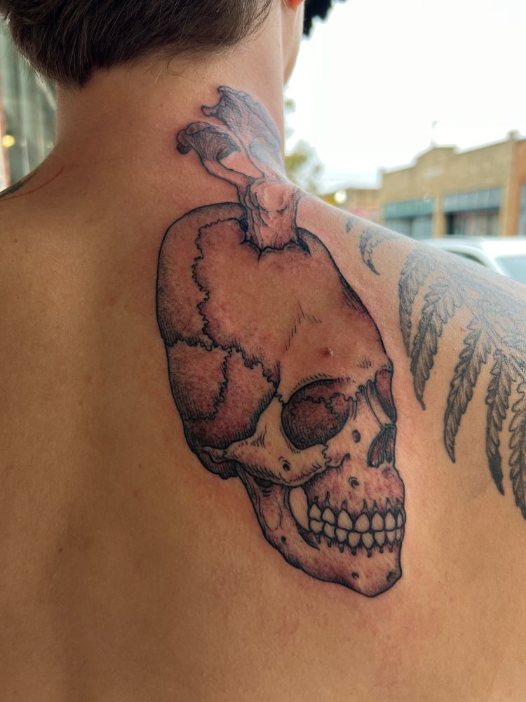 Back tattoo of a Long skull, perhaps of alien ancestry, sprouting forth chanterelle mushrooms upon the neck