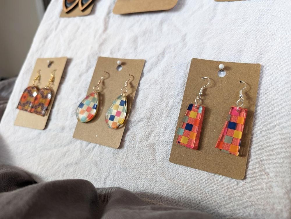 A corkboard wrapped in a white cloth holds various colorful handmade acrylic and leather earrings