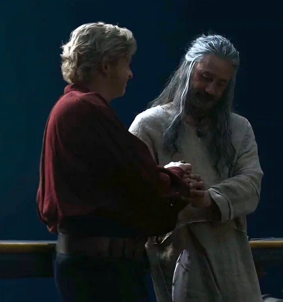 Ed and Stede clasping hands in S2E5 of OFMD. Stede is wearing a red silk shirt and Ed in wearing a rice sack onesie.