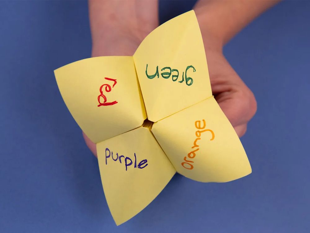 Hands holding a folded paper fortune teller with colors written on each quadrant 