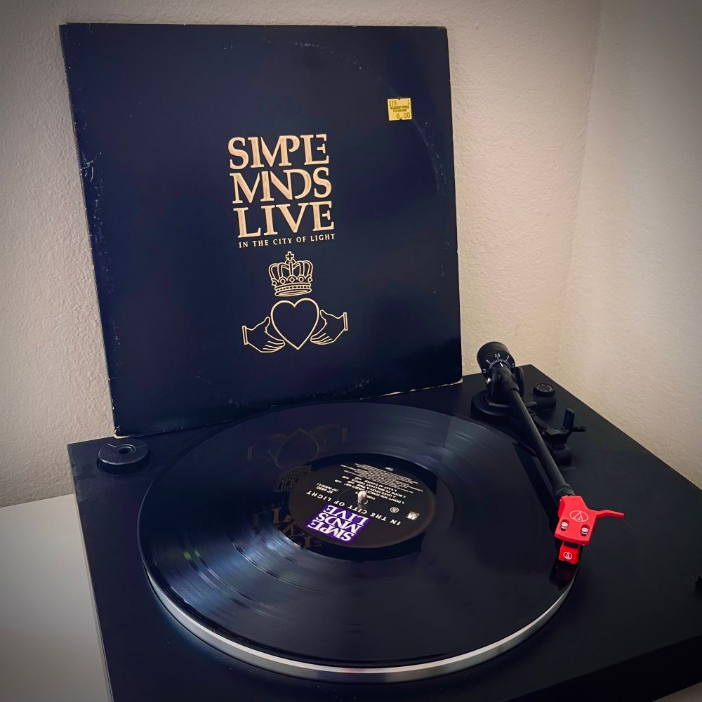 Vinyl copy of Simple Minds Live in the City of Light on a record player with the sleeve propped behind it 