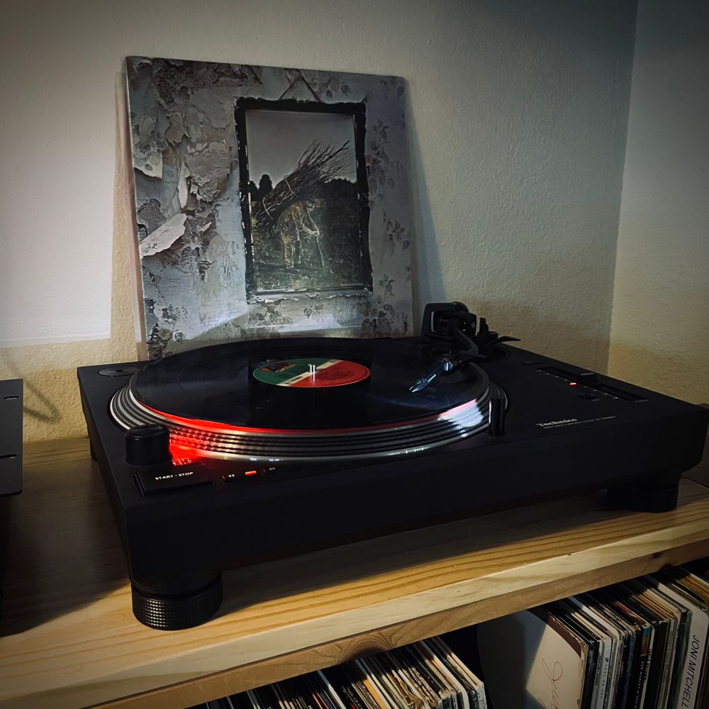 Vinyl copy of Led Zeppelin IV playing on a record player with the cover propped behind depicting a picture of a man carrying a bundle of sticks 