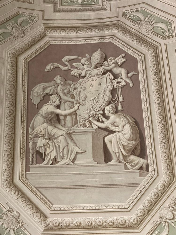A framed ceiling painting with 3 figures holding a Papal insignia in beige tones