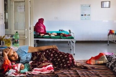 A woman rests next to her newborn baby in a bed in a hospital.

Credit: Morsa Images