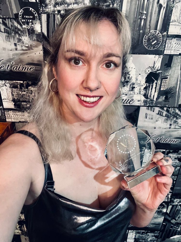 Blonde-haired woman in a silver dress holding a ‘Most Supportive’ award