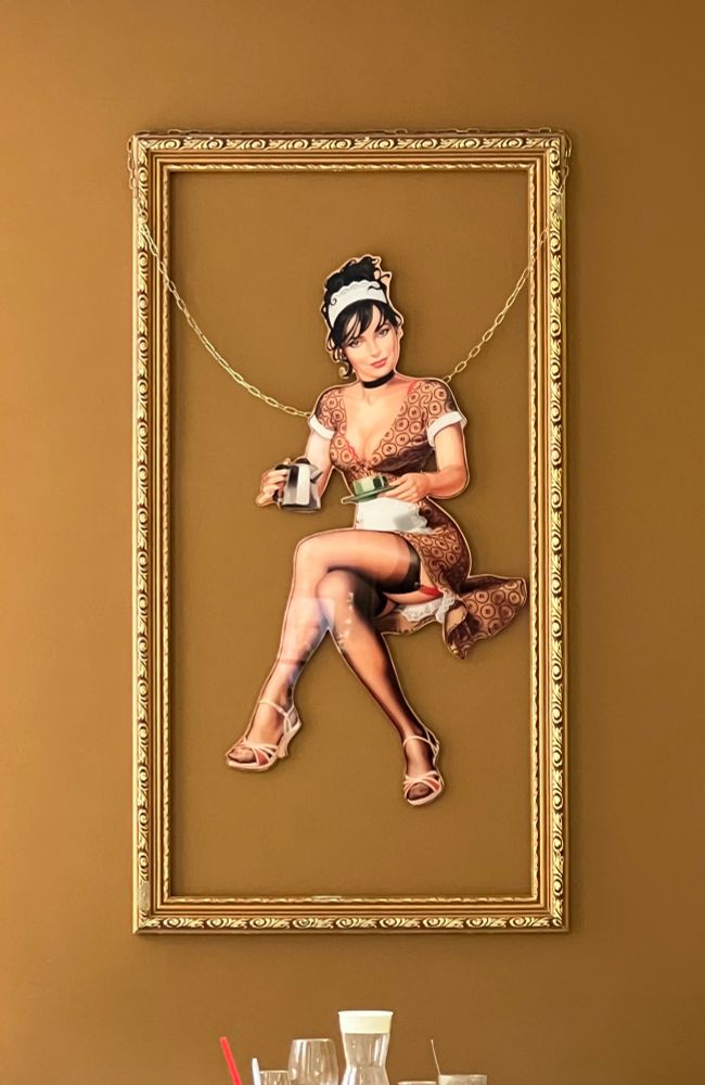 Ausgeschnittener Pappaufsteller mit sexy Kellnerin an einer Kette in Bilderrahmen aufgehängt 