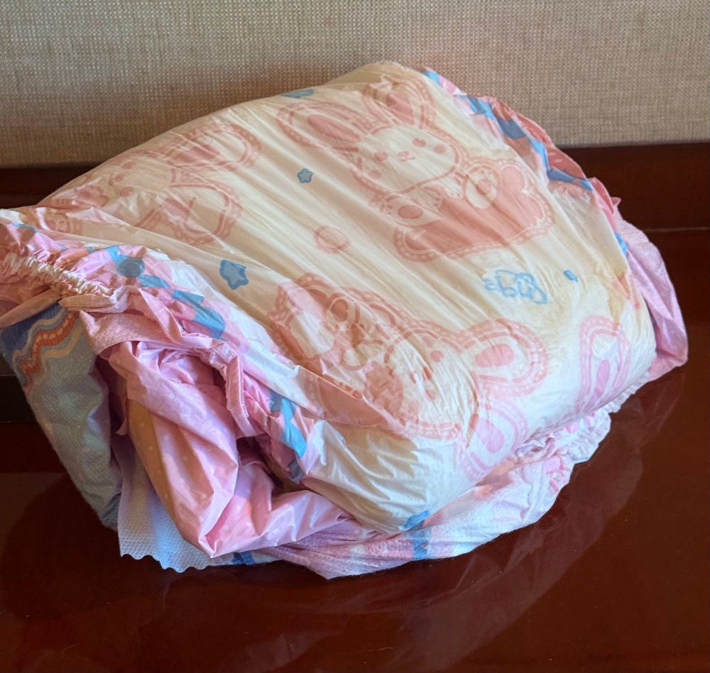 A soaked and folded abu bunnyhopps diaper, on a reflective polished wood shelf. It looks very squishy.