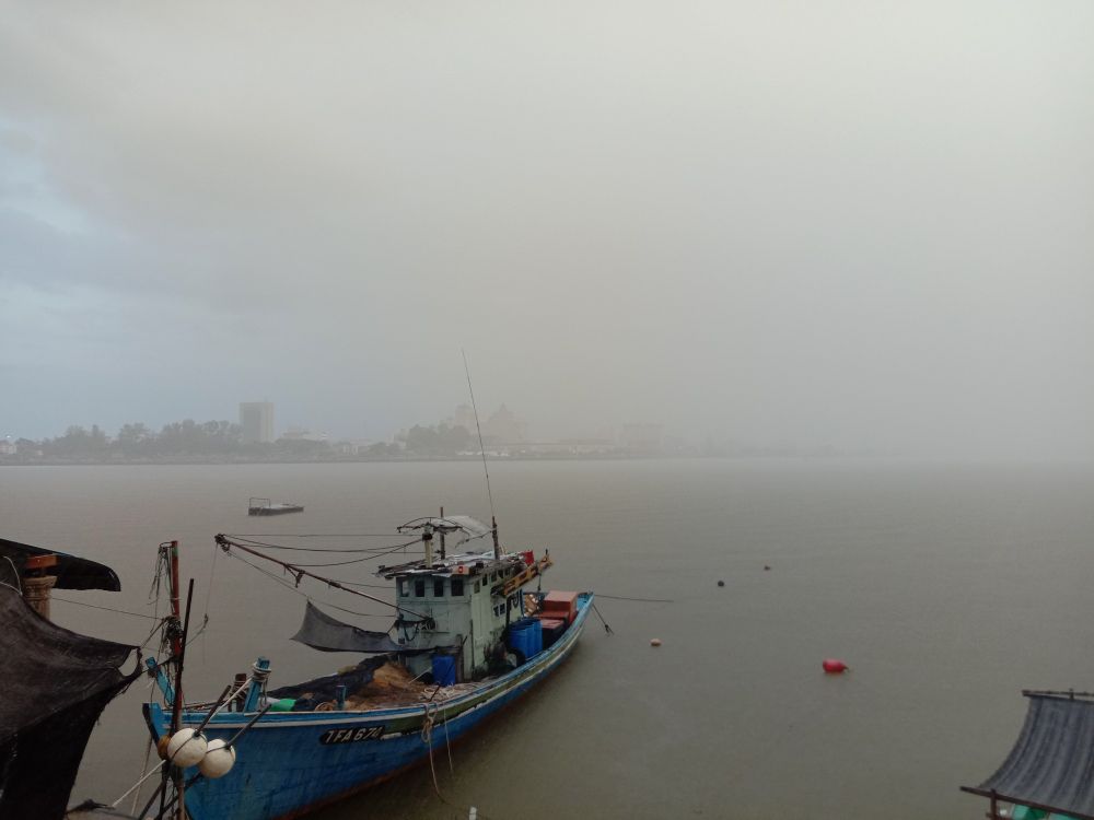 Alt Text: A fishing boat during a heavy downpour on a river with low visibility, creating a mystical mist-like atmosphere.