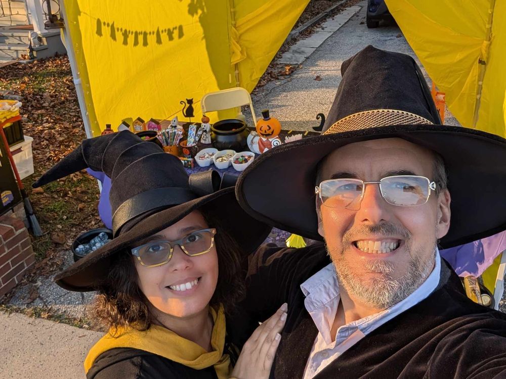 Melissa and Charlie in front of a big yellow tent on Halloween dressed as a witch and wizard.