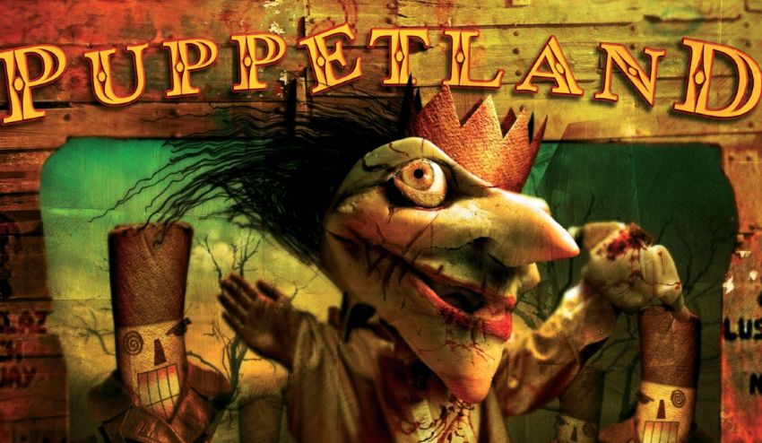The cover of the book Puppetland with Punch the Maker Killer on the cover. It's a puppet with a cracked face, a long nose, bulging eyes, and red lips. There is whispy black hair flowing out the back and a gold crown on his head with a couple of soldier looking puppets behind him.