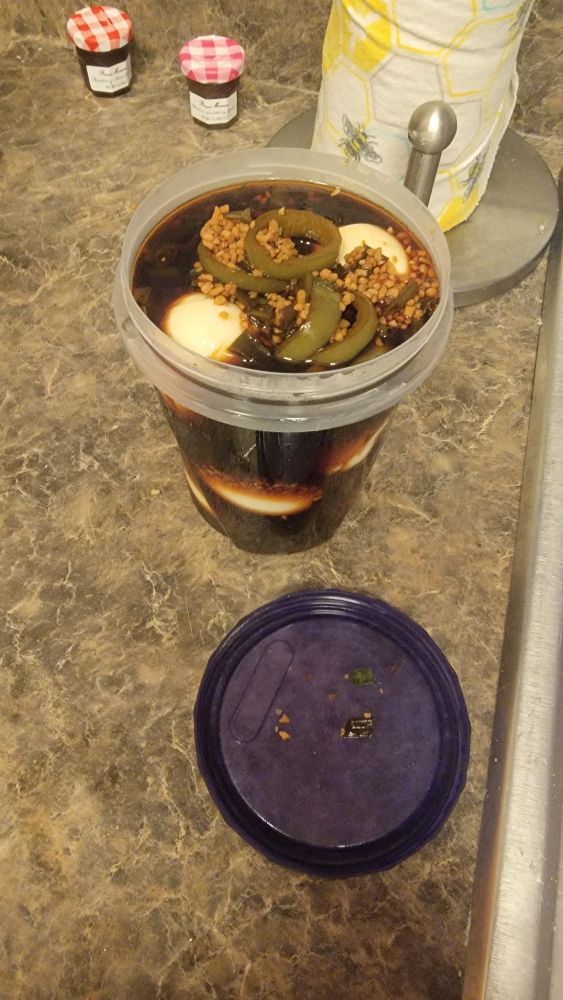 Tupperware container filled with hard boiled eggs in a brine of soy sauce, rice vinegar, garlic, jalapeños, and green onions.