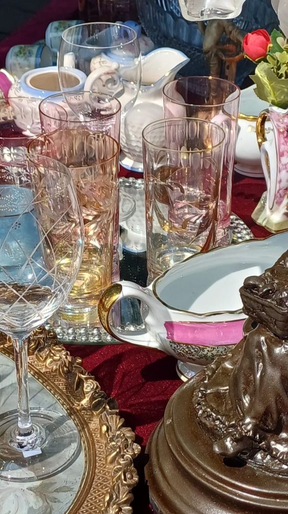 Copos, taças, molheiras, xícaras e porcelanas diversas sobre uma toalha vermelha.