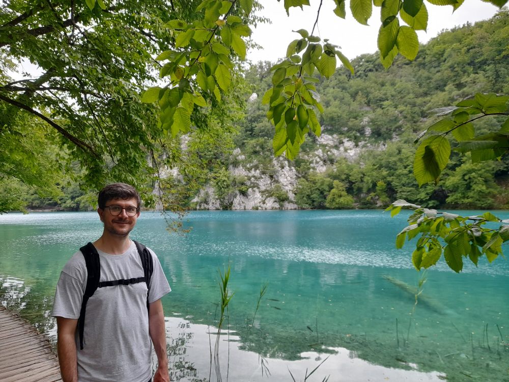 Matthew standing smiling at the camera in front of a turquoise-coloured lake in Plitvice Lakes National Park, Croatia