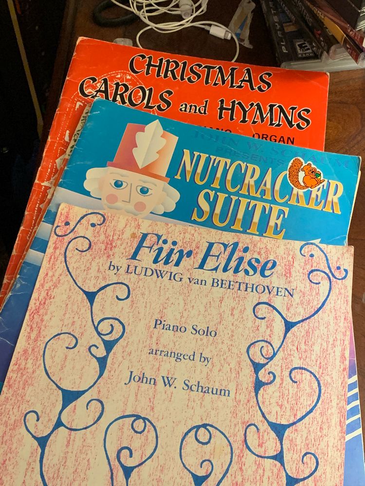 Scores for “Christmas Carols and Hymns”, “Nutcracker Suite” and “Für Elise” on an end table. There are also headphones and some video games visible.