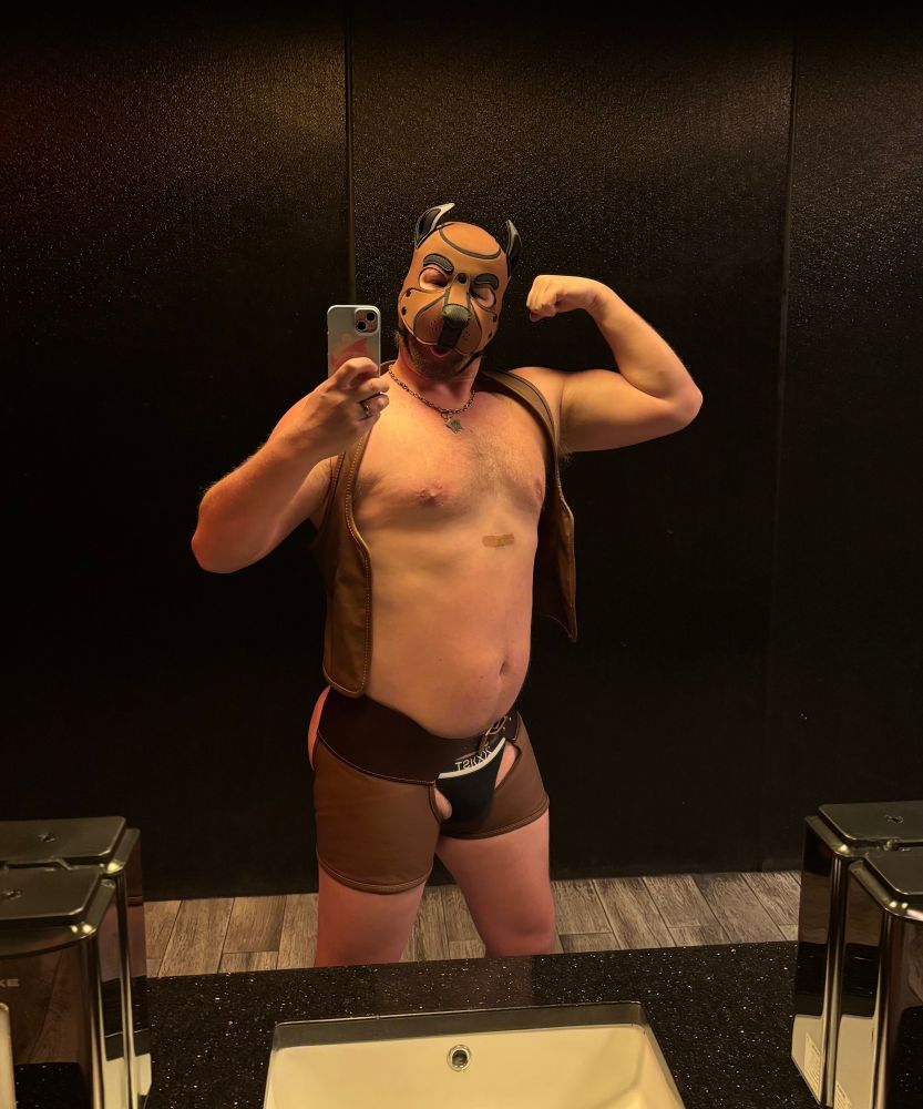 Musky Cub Rye in brown leather and pup hood showing flexed bicep