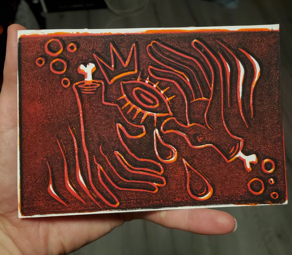 Block print of two severed hands surrounding an eyeball  in black and red and orange 