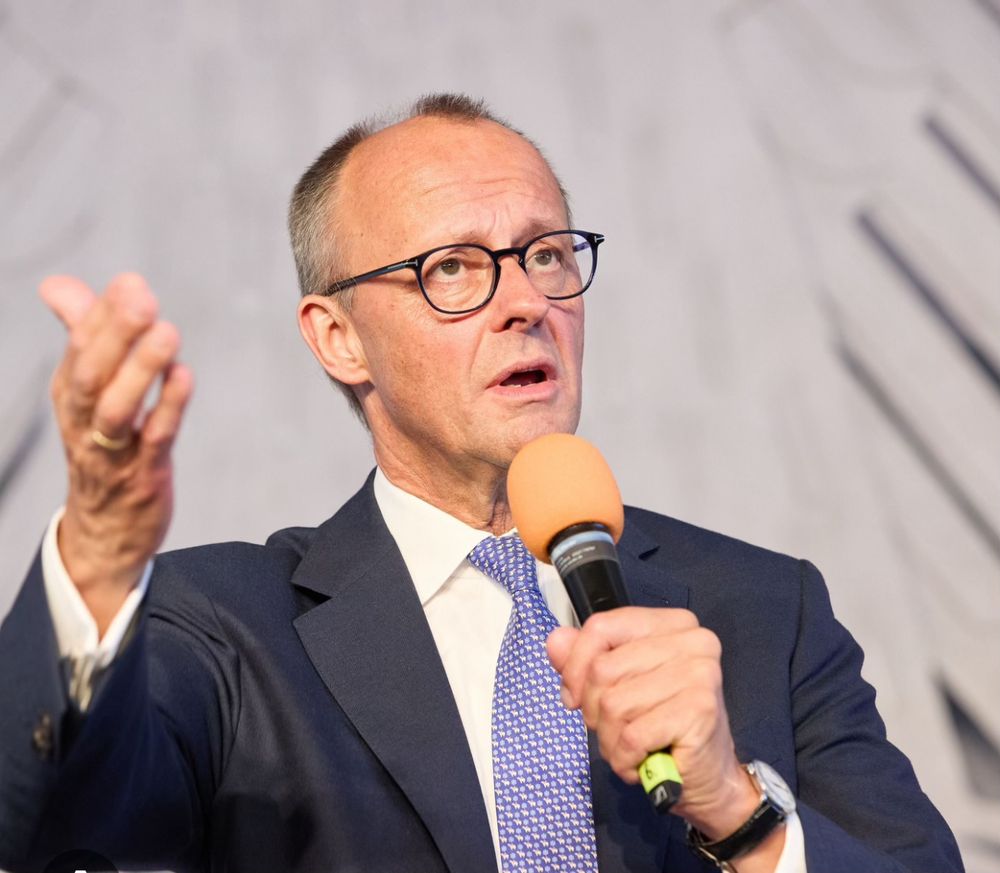 Merz spricht ins Mikrofon, man könnte bei der Geste auch glauben er würde singen