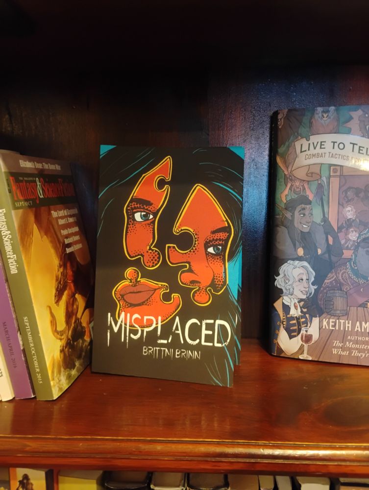 A front facing copy of Misplaced by Brittni Brinn on a wooden bookshelf between sci-fi and fantasy books.
