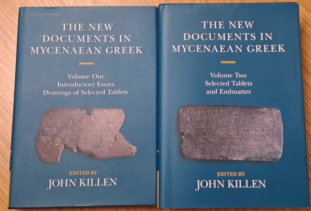 Two large volumes of "The New Documents in Mycenaean Greek", edited by John Killen, each with a photograph of a Linear B tablet on the cover. Volume 1: Introductory Essays and drawings of selected tablets; volume 2: selected tablets and endmatter