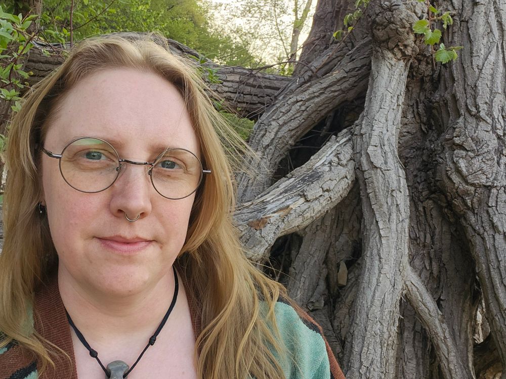 The author of this post taking a selfie in front of the root gnarled base of a tree.