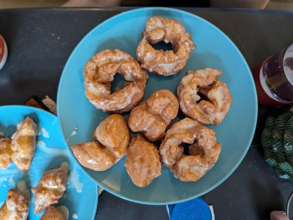A plate with an assortment of glazed crullers and beignets. There's a second plate with more beignets off to the side 