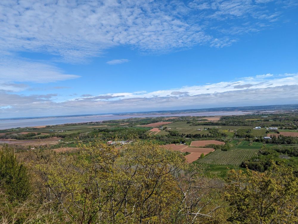 View from a cliff over some farm fields and then water in the background.