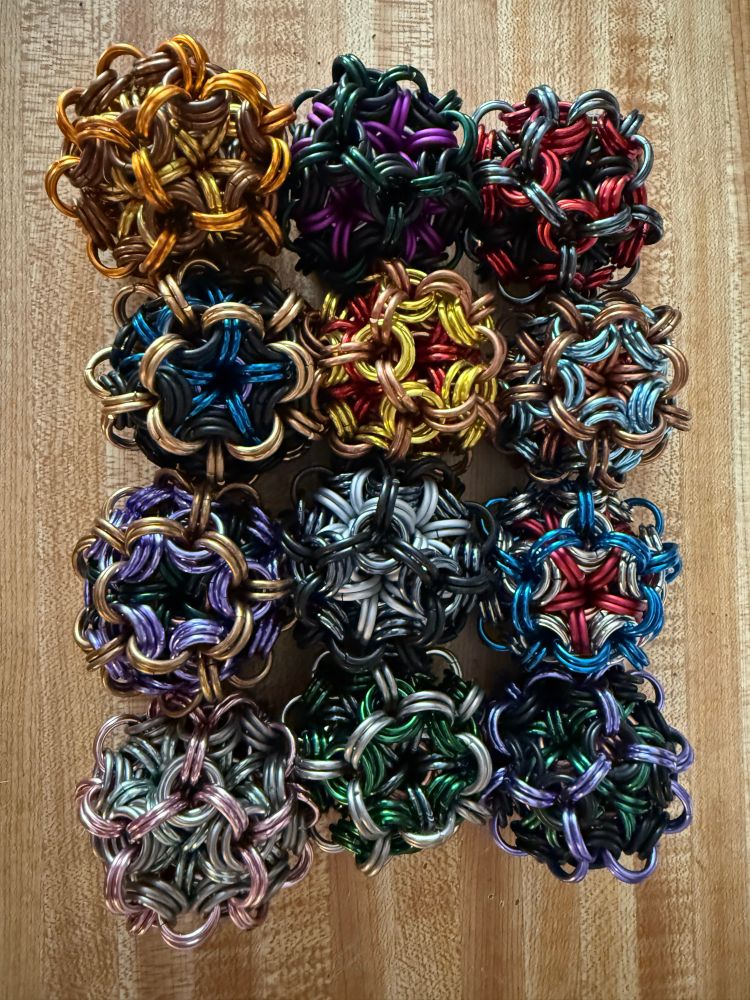 A series of colorful chainmaille juggling balls on a wood background
