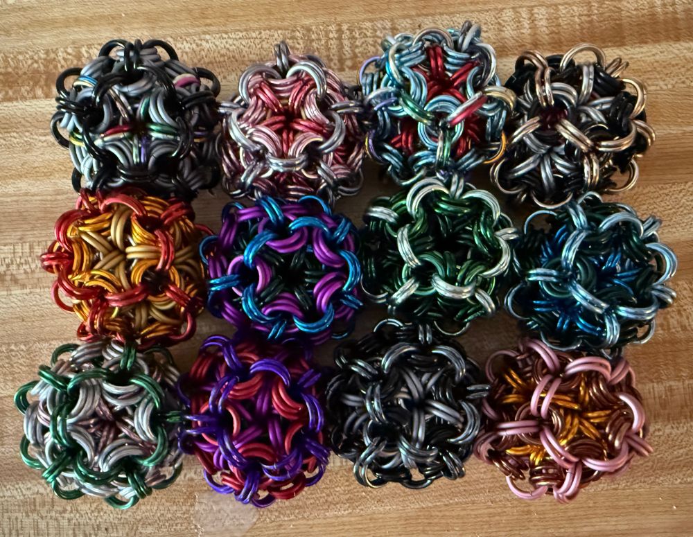A variety of colorful balls made of chainmaille rings on a wood background.