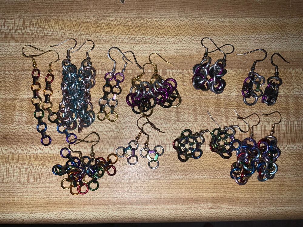 A variety of chainmaille earrings on a faux wood background