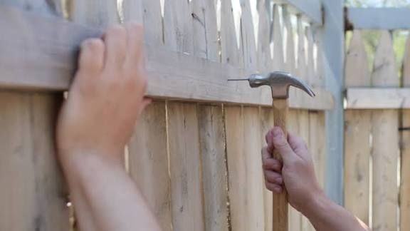 Photo of hands hammering a nail into a fence