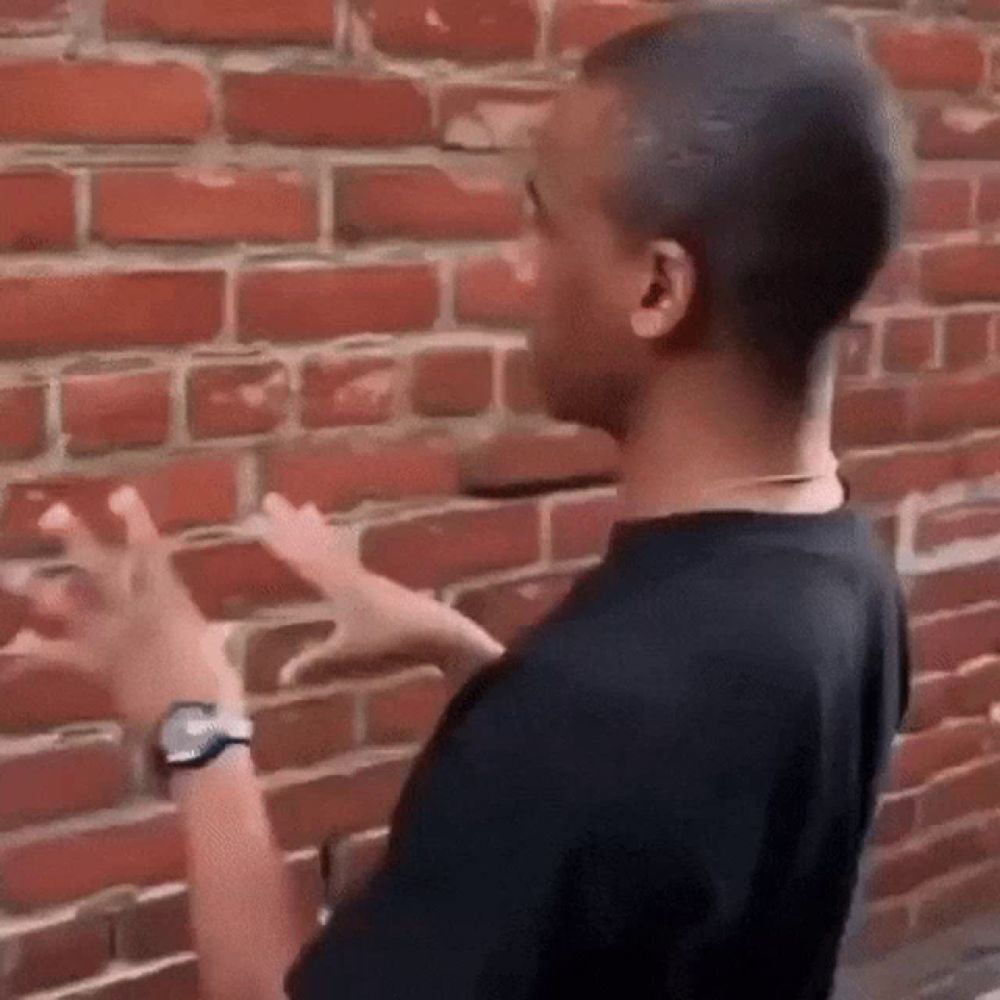 a man in a black shirt is pointing at a brick wall .