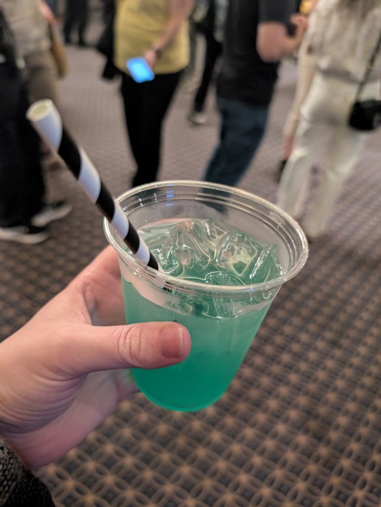 My have with a cup of a green boozy drink with a black and white striped straw.