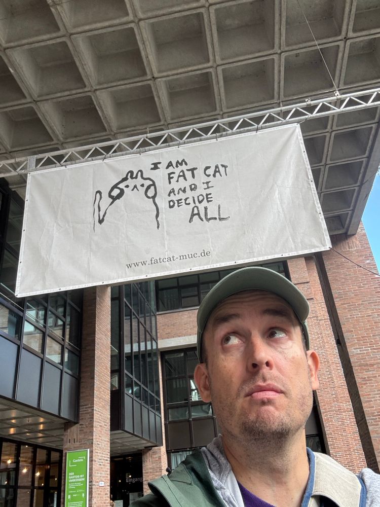 Me beneath a sign that reads I AM FAT CAT AND I DECIDE ALL. I’m in Munich btw