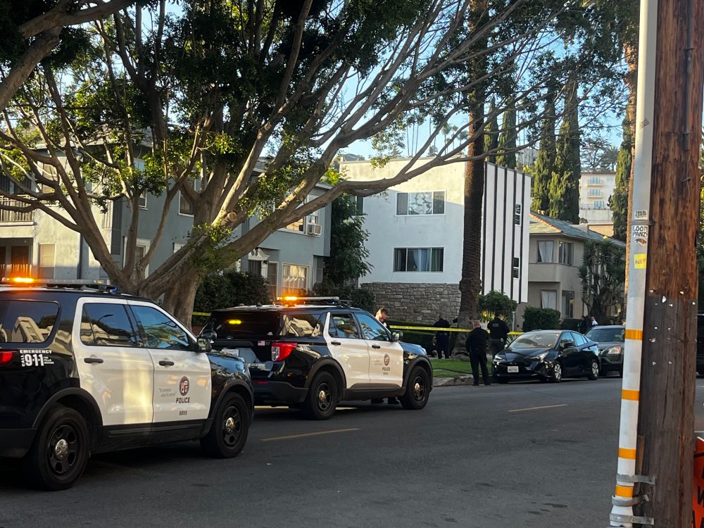 LAPD police cruisers in front of a two-story apartment with crime scene tape
