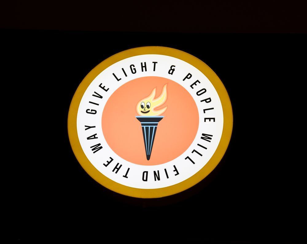 A circular art piece which reads, 'Give light & people will find the way'. In the center, there is a a Carnegie inspired flaming torch.